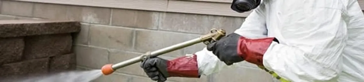 Pest control technician applying exterior insect treatment along a home foundation in Yonkers, NY