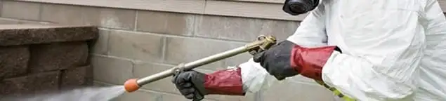 Pest control technician applying exterior insect treatment along a home foundation in Yonkers, NY