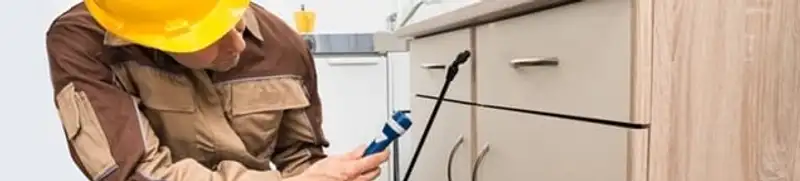 Roach exterminator applying treatment under kitchen cabinets in Yonkers, NY