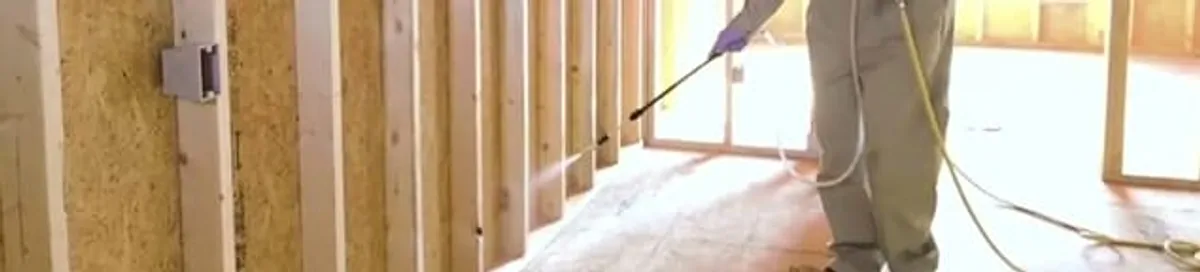 Termite treatment technician applying spray along framing and unfinished walls in Yonkers, NY
