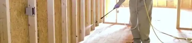 Termite treatment technician applying spray along framing and unfinished walls in Yonkers, NY